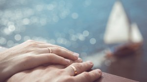 Holding Hands with wedding rings on the background of sea and sun – shutterstock_167534945