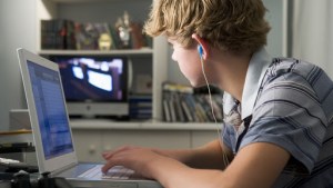 Young boy in bedroom using laptop and listening to MP3 player – es