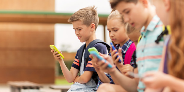 web3-primary-education-friendship-childhood-technology-and-people-concept-group-of-happy-elementary-school-students-with-smartphones-and-backpacks-sitting-on-bench-outdoors-shut