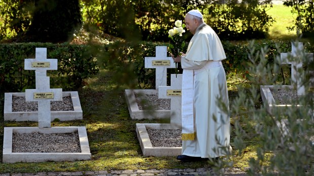 Pope Francis stands by graves with flowers at the French military cemetery