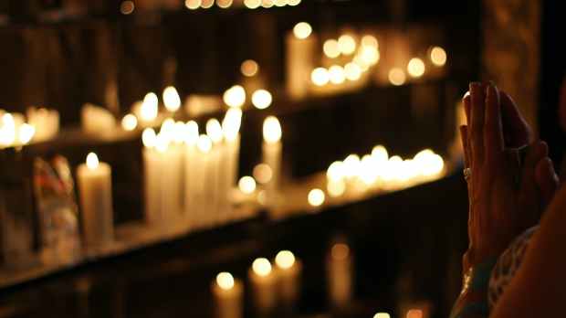 close up photograph of person praying in front lined candles