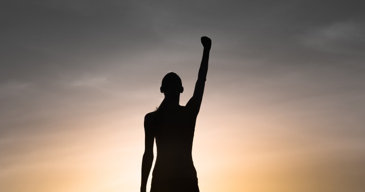 Strong, victorious , and motivated young woman raising her fist up to the sunset sky