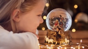 Girl looking at a glass ball with a scene of the nativity of Jesus Christ in a glass ball on a Christmas tree
