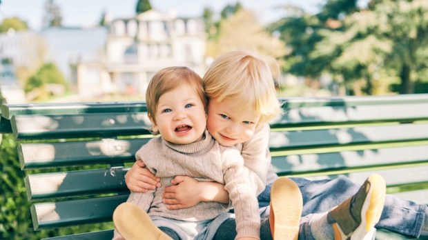 two adorable siblings resting on the bench in sunny park
