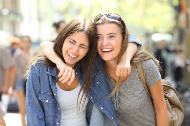 Two funny friends laughing loud walking in the street